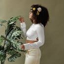 Stylish woman with afro hair and floral decor poses among lush green plants, showcasing modern fashion.